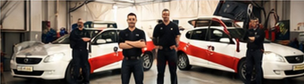 Kelly Auto Repair technicians standing together in front of service vehicles at the Denver shop